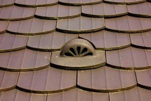 A matching roof vent in the midst of brown shingles.