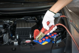 Man holds jumper cables inside a car.