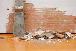scraper laying next to wall with pile of paint chips below