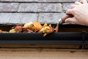 hand scooping leaves out of roof gutter with tool