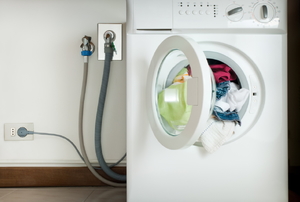 Hoses and and cords connect a washer to a wall.
