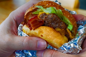 two hands holding a burger in tinfoil