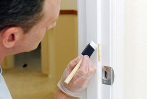 A man touching up paint on a door.