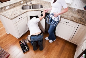 A couple working on a DIY project underneath a kitchen sink.