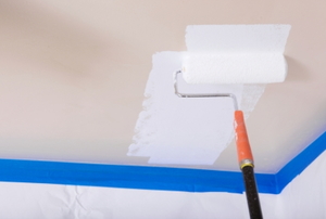 a paint roller adding white paint to a ceiling