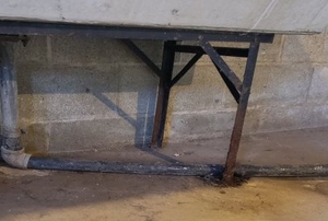 A sink in a basement with a pipe leading to a drain in the floor.