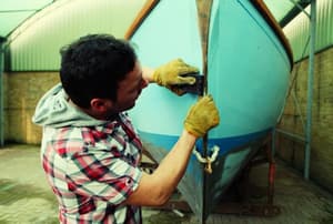 A boater cleaning the bow of an old sailing boat.