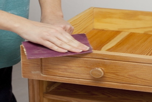 A woman works on an antique cabinet door.