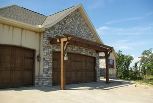 A wood pergola or arbor in front of a house over the garage door. 