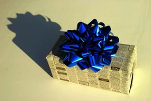 A Christmas present wrapped in newspaper, with a blue bow on top.