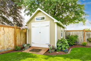 A small wooden storage shed with a ramp in a backyard.