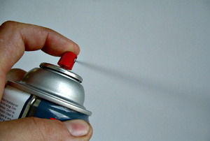 A finger pushing down the button on a can of spray paint.