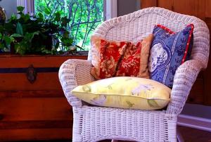 A white, wicker chair covered in throw pillows.