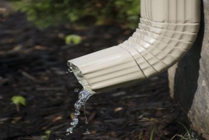A downspout next to a house draining water into the ground.