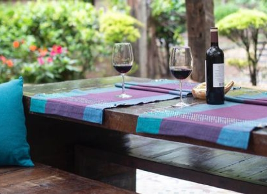 backyard patio with dark wooden table, wine glasses and bottle, and blue and purple fabrics