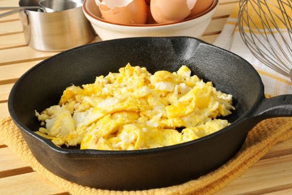 A cast iron skillet with scrambled eggs in it. 