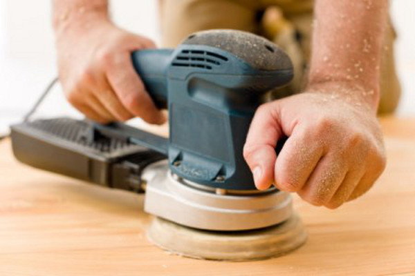 An orbital sander being used on some plywood. 