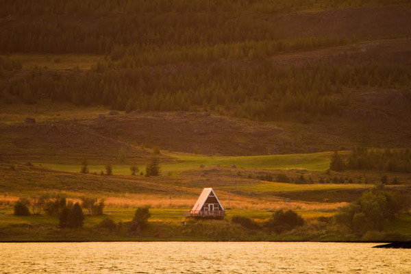 A-frame house in the countryside in front of a lake. 