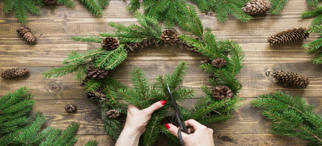 Someone adding pinecones to a holiday wreath.