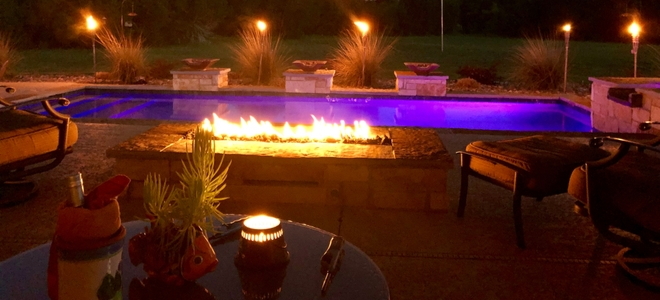 swimming pool with fire pit and torches at night