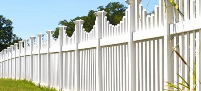 A white fence with plants and grass surrounding it.
