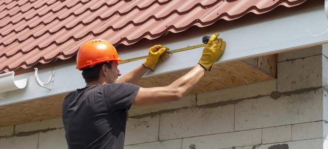 A man in a hardhat measuring a roofline for a gutter installation.
