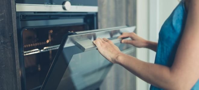 A woman opens an oven door.