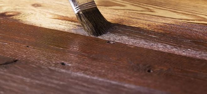 A dark wood flooring stain being applied with a paint brush.
