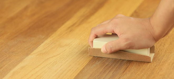 A hand sanding a wood floor. 