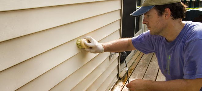 A man cleaning vinyl siding on a house. 