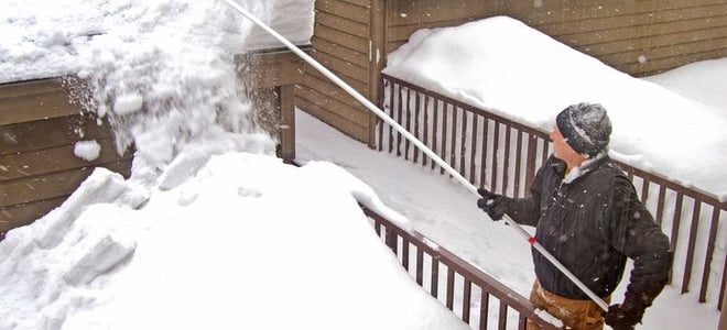 A man removing snow from a roof with with roof rake. 
