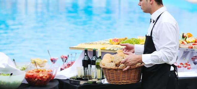 A caterer setting food out on a table next to a pool. 
