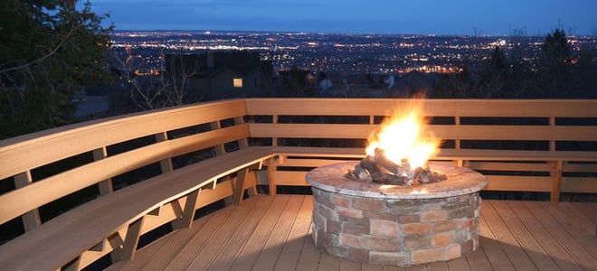 A fire pit on a deck with a view of lights. 