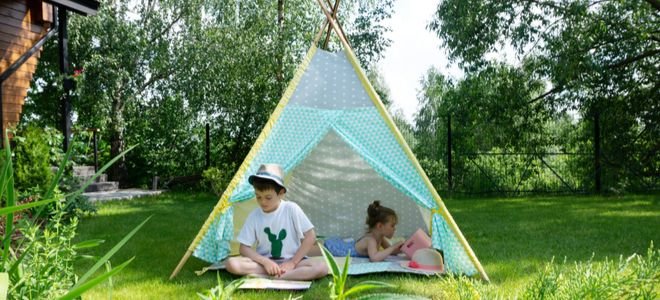 kids relaxing in a teepee made with patterned sheets in an outdoor area