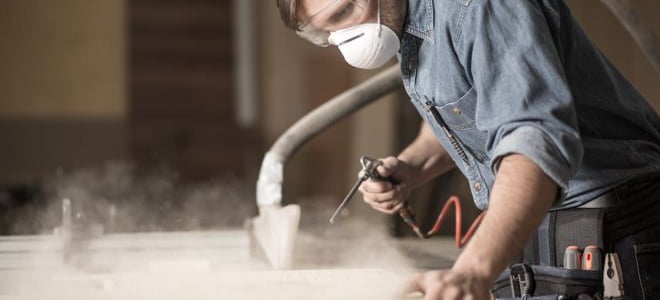 A man working on wood in a workshop with a dust mask and ear protection. 