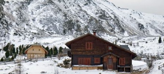 A vacant summer hosts sits in snow with mountains in the background.