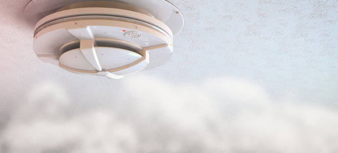 A fire detector in a ceiling surrounded by smoke. 