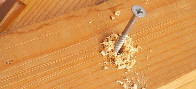 A screw in a piece of lumber with sawdust spilling out. 