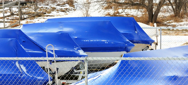 A row of boats covered in tarps surrounded by snow. 
