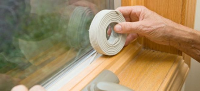 A person installs weatherstripping to a window.