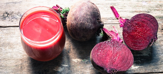 A cup of beet juice on a wood background with beets next to it. 