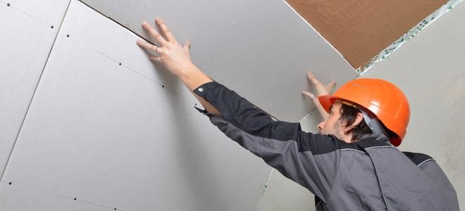 Person installing drywall on a ceiling