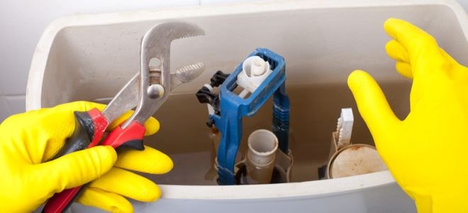 gloved hands fixing open toilet tank with plumbing wrench