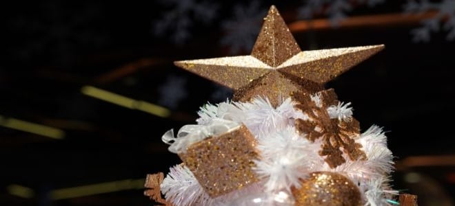 Gold glitter star and ornaments on top of a white Christmas tree
