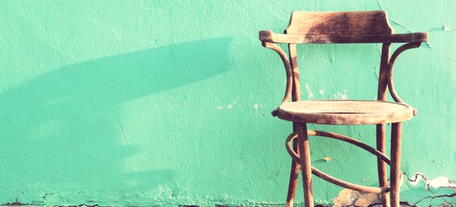 A broken wooden chair against a mint green wall.