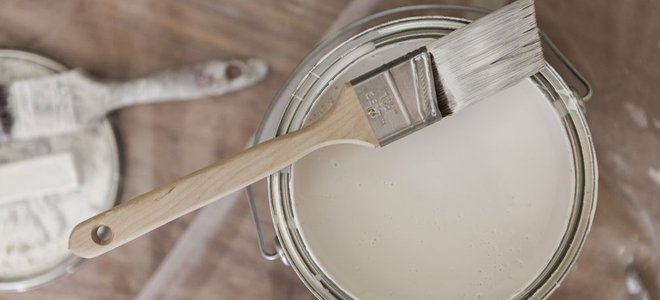A can of white paint with a brush resting on top.