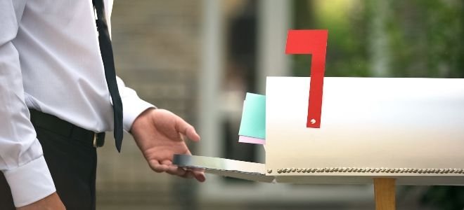 person in shirt and tie opening a mailbox with the flag up and mail sticking out