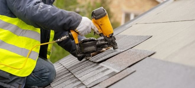 person shingling roof with nail gun