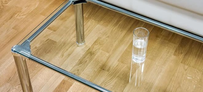 A glass coffee table with a cup of water on it. 