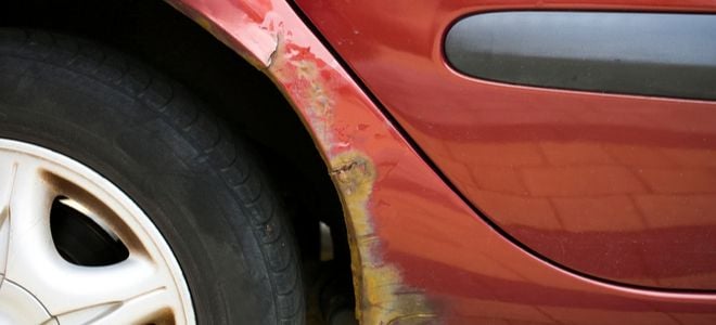red car with paint damage and rust near tire